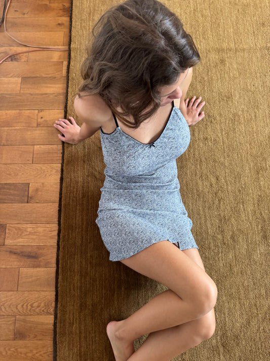An image taken from above of a woman with brown hair sitting on a light brown rug on floorboards. She is leaning back on her hands, wearing the Lola Mini Dress in Midnight Floral by Juem. Her feet are bare.