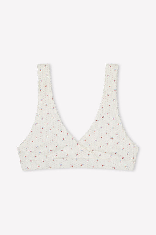 The Bernie Bra - Flora is a cream-colored, ribbed cotton triangle bra featuring a subtle pink floral pattern and supportive underbust wrap-style front, shown on a plain white background.