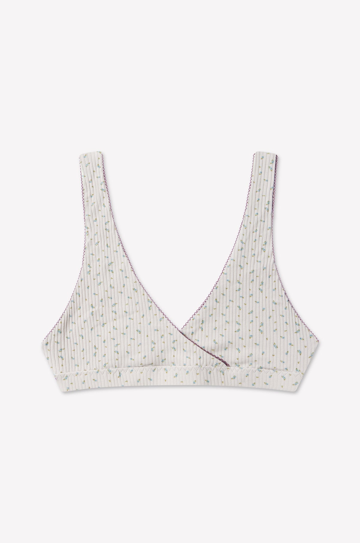 The Bernie Bra - Blue Floral by 0 features a soft cotton triangle bralette design with a crossover front. It has a white base decorated with thin vertical stripes and a delicate blue floral pattern, accented by purple stitching along the edges. Designed for comfort, it offers supportive underbust construction without any padding or underwire.