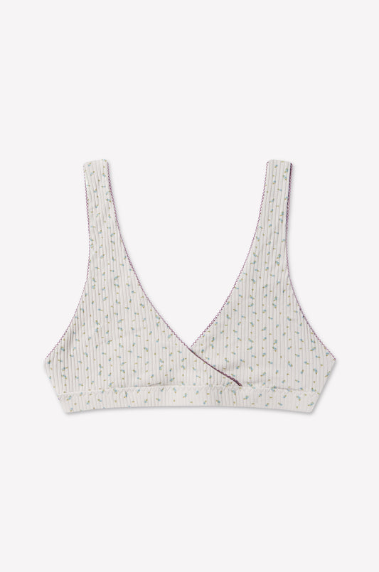 The Bernie Bra - Blue Floral by 0 features a soft cotton triangle bralette design with a crossover front. It has a white base decorated with thin vertical stripes and a delicate blue floral pattern, accented by purple stitching along the edges. Designed for comfort, it offers supportive underbust construction without any padding or underwire.