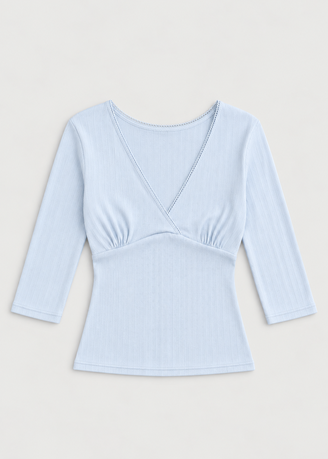 The Fern Top - Glacier Blue by Juem laid flat on a cream background, a soft pointelle knit top with a v-neck crossover front, gathered bust panel and 3/4 sleeves.