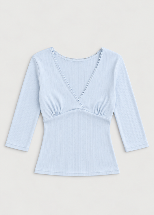 The Fern Top - Glacier Blue by Juem laid flat on a cream background, a soft pointelle knit top with a v-neck crossover front, gathered bust panel and 3/4 sleeves.