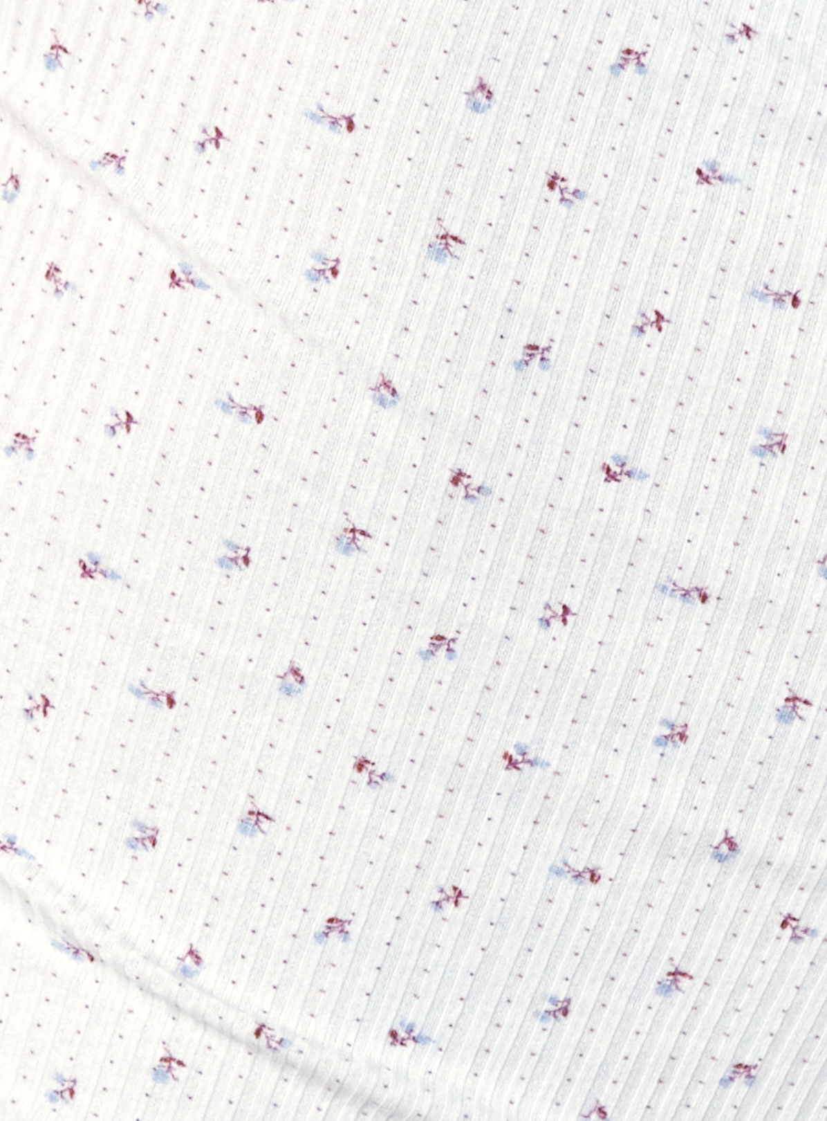 The Effie Tee - Flora is made from white GOTS organic cotton with subtle vertical stripes and small blue and red floral motifs. Its soft, slightly wrinkled texture delivers the signature comfort of the Effie Tee design.