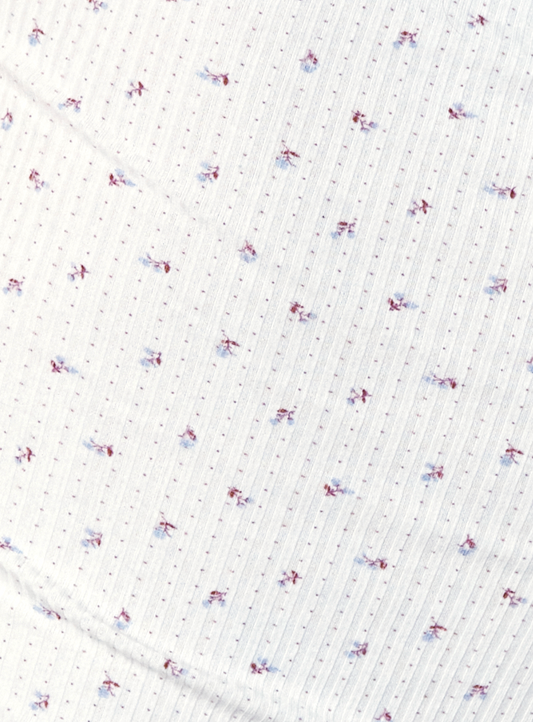 The Effie Tee - Flora is made from white GOTS organic cotton with subtle vertical stripes and small blue and red floral motifs. Its soft, slightly wrinkled texture delivers the signature comfort of the Effie Tee design.