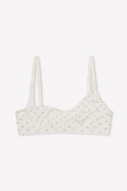 The Jane Maternity Crop - Flora is a white scoop neck bralette with thin adjustable straps, ribbed texture, and pink floral print. Made from organic cotton, it offers a seamless design and front clasp for comfort.