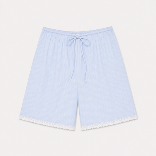 The Mae Short - Cloud Stripe by 0 features light blue, knee-length organic cotton with white pinstripes, an elastic drawstring waistband, and white lace trim at the hem. Shown laid flat on a white background.