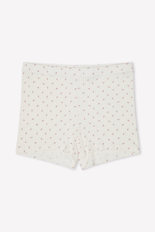 The Maggie Short - Flora is an off-white, organic cotton short featuring a ribbed, mid-rise fitted style and a subtle pink floral print, shown against a plain white background.