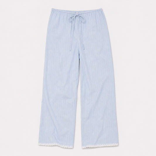 The Josephine Pant - Cloud Stripe by 0 features light blue organic cotton with thin white stripes, an elastic drawstring waist, relaxed straight leg, and white lace-trimmed hem, shown laid flat on a white background.